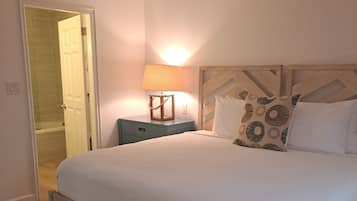 A bedroom with a bed, a nightstand, a lamp, a ceiling fan, and a door leading to a bathroom.