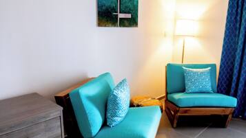 A room with two teal armchairs, a wooden side table, a floor lamp, and a painting on the wall.