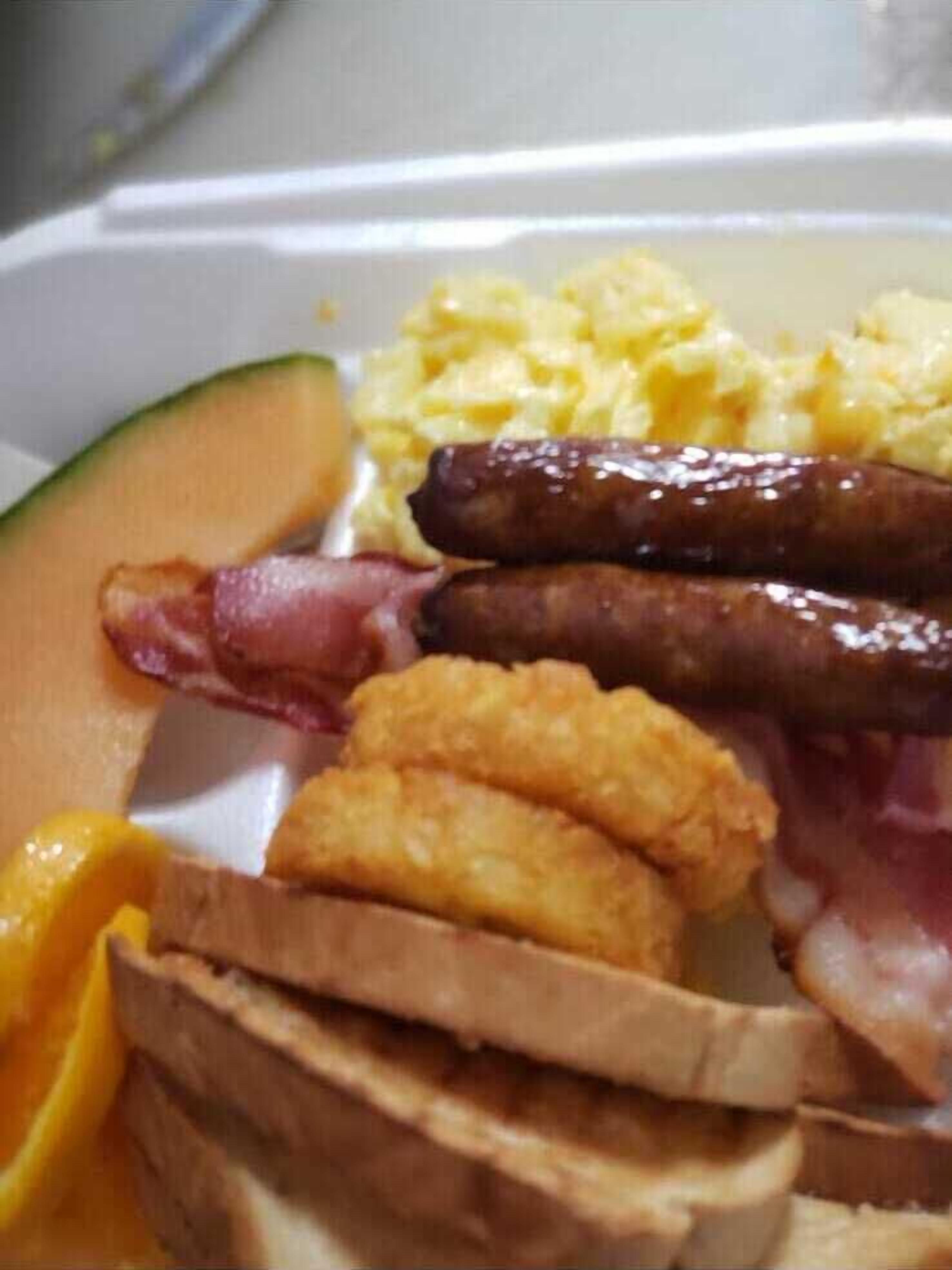 A meal with toast, sausage, eggs, and a slice of melon.
