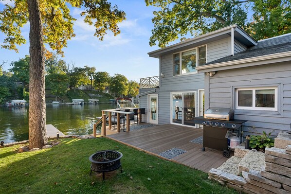 A house with a deck, a grill, and a fire pit. - Three steps away from the water on beautiful Okauchee Lake! (Okauchee Lake)