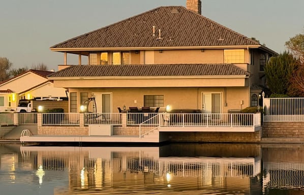 A two-story house with a balcony, a swimming pool in front, and a car parked nearby.