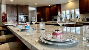 Une cuisine spacieuse avec des meubles en bois, un plan de travail en marbre et un îlot central sur lequel sont disposés un gâteau et des verres.