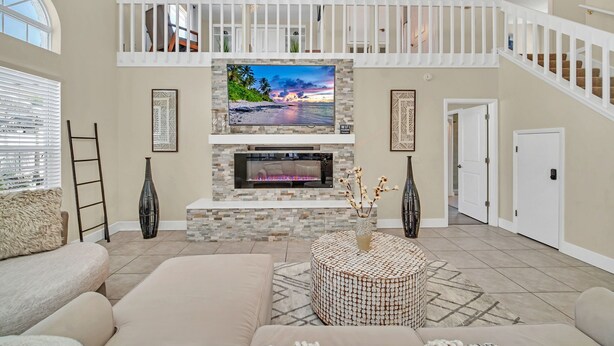 A spacious living room with a fireplace, a large flat-screen TV mounted above it, a comfortable sofa, and a staircase leading to an upper level. - Welcome to Alena's Place! Only minutes away from Disney! (Kissimmee)