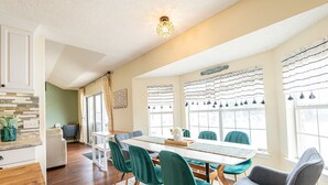 Een eetgedeelte met een lange tafel, teal stoelen en een keuken op de achtergrond.
