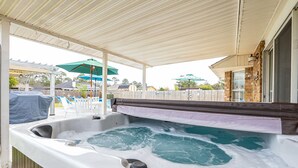 Een hottub onder een overdekte patio, met een houten hek en parasols op de achtergrond.