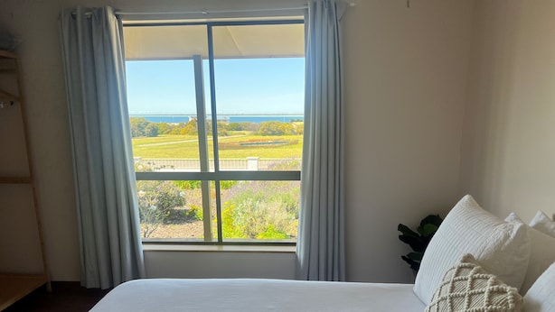 A bedroom with a large window, a bed with white bedding, and a view of a green landscape. - Captain's Quarters ~ Pet Friendly - Off Peak Special! (Point Turton)