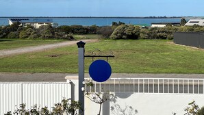 A coastal view with a grassy area, a white fence, and a building with solar panels. - Captain's Quarters ~ Pet Friendly - Off Peak Special! (Point Turton)
