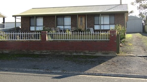 A single-story brick house with a green roof, a white fence, and a small garden area. - Captain's Quarters ~ Pet Friendly - Off Peak Special! (Point Turton)
