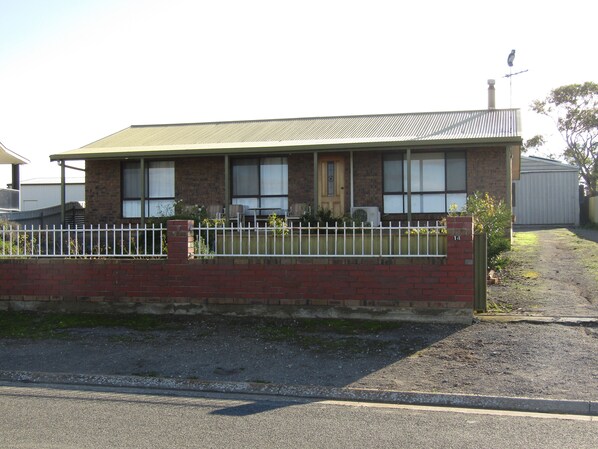 A single-story brick house with a green roof, a white fence, and a small garden area. - Captain's Quarters ~ Pet Friendly - Off Peak Special! (Point Turton)