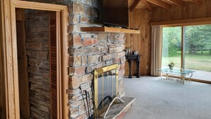 A stone fireplace with a TV above it, a glass table, and a view of the outdoors. - Lake Michigan Retreat (Menominee)