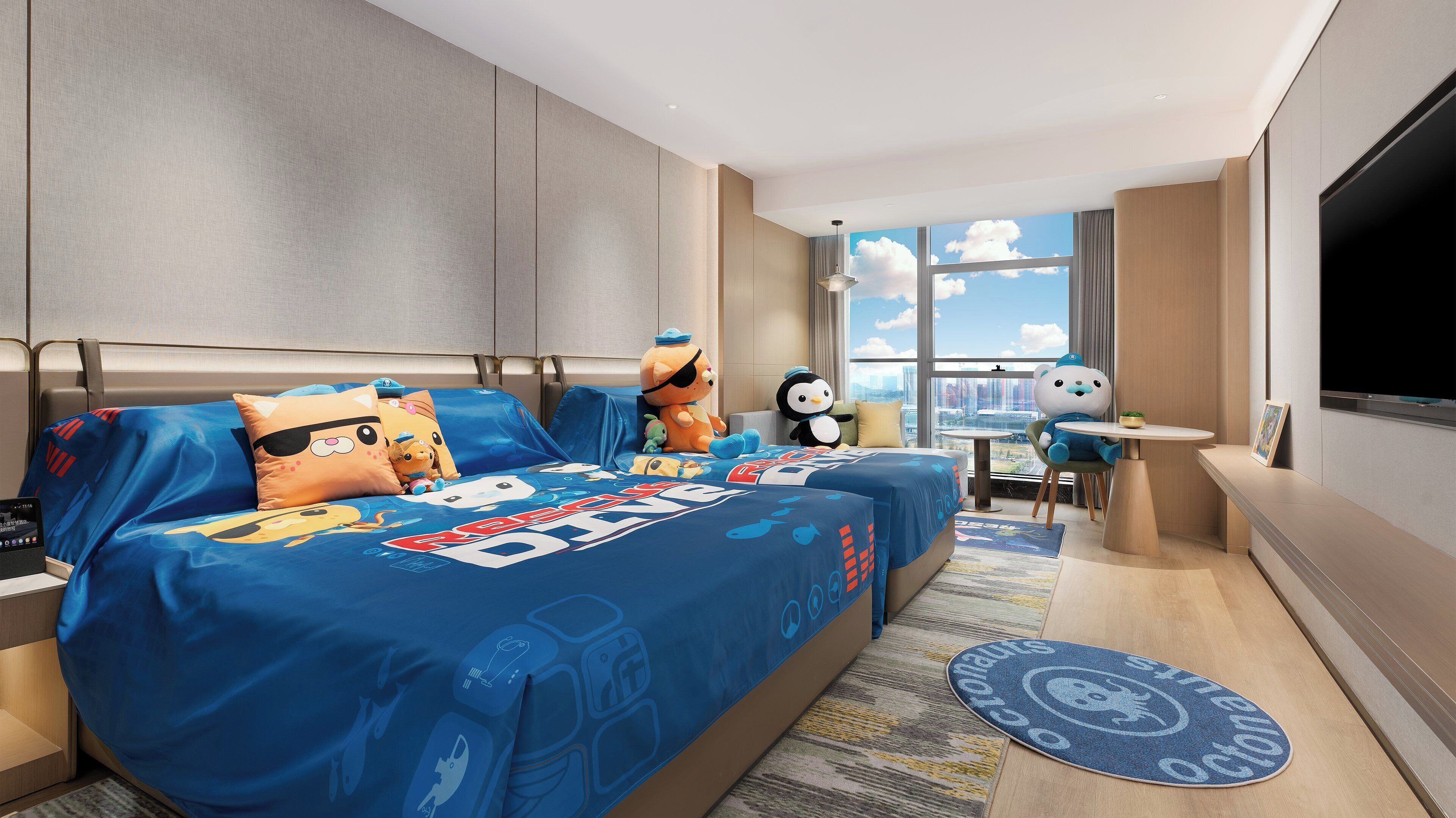 A hotel room with a large bed, a desk, a chair, a TV, and a view of the city.