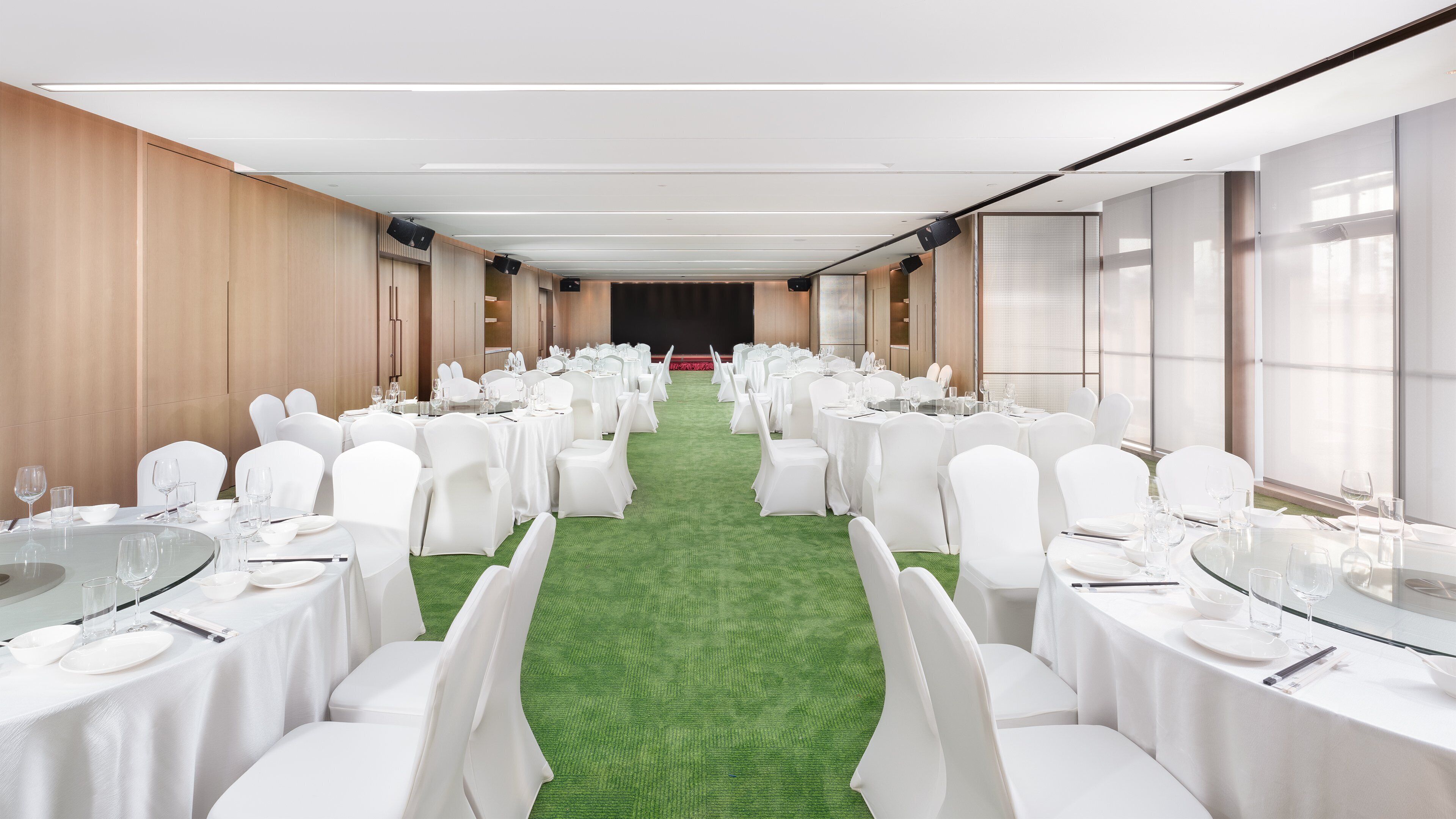 A conference room with round tables, white chairs, and a green carpet.