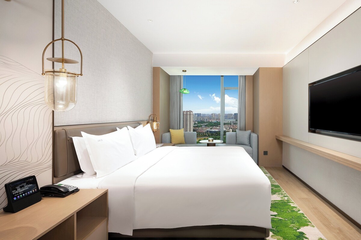 Een moderne hotelkamer met een groot bed, een flatscreen televisie, een bureau met telefoon en uitzicht op de stad.