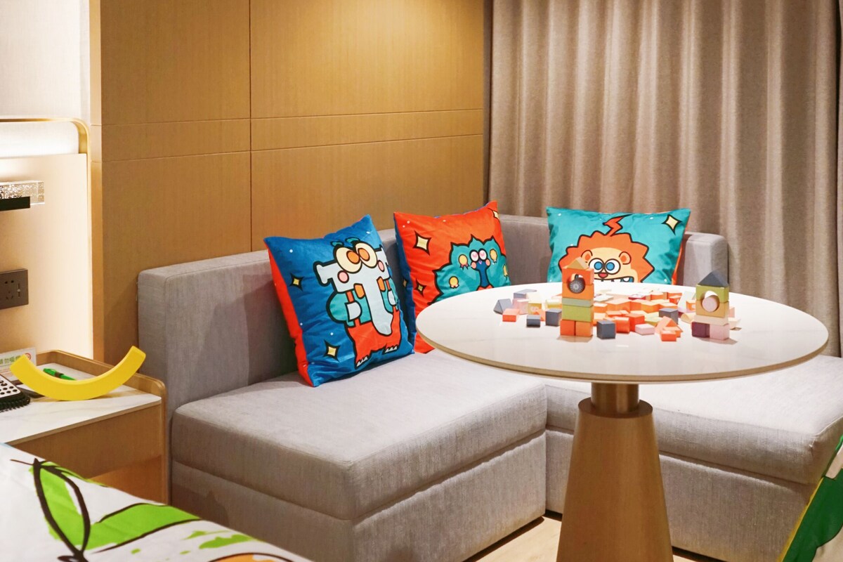 A modern hotel room with a sofa, a round table with building blocks, and a hanging light fixture.