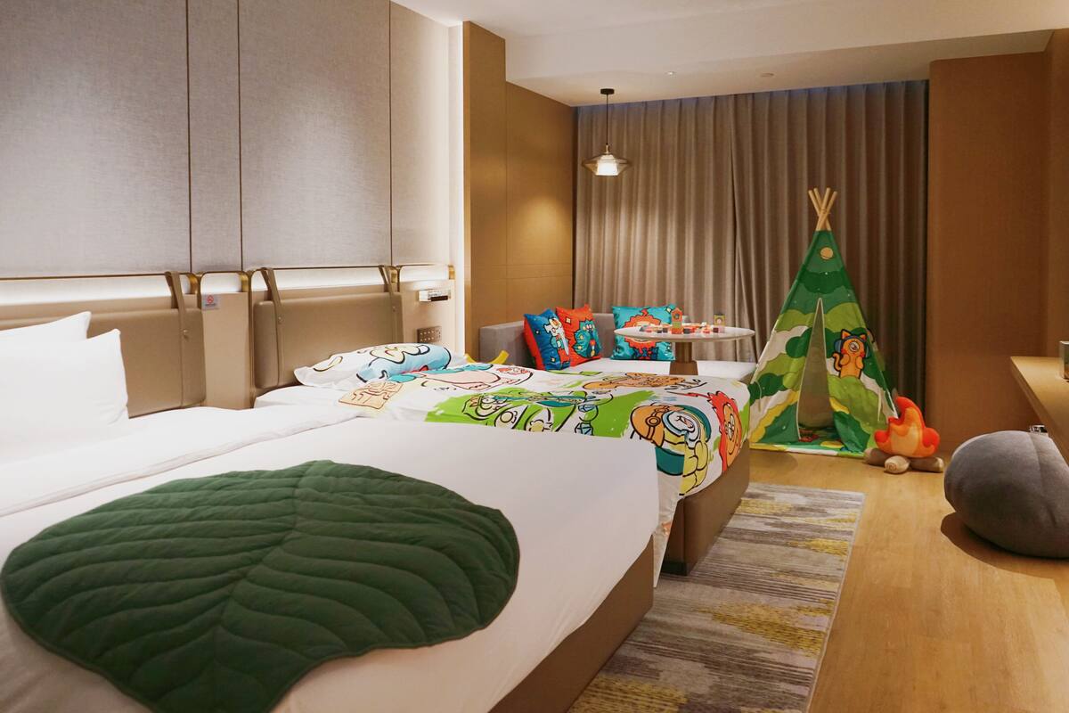 A hotel room with a large bed, a sofa, a small table, a teepee, and a grey bean bag.