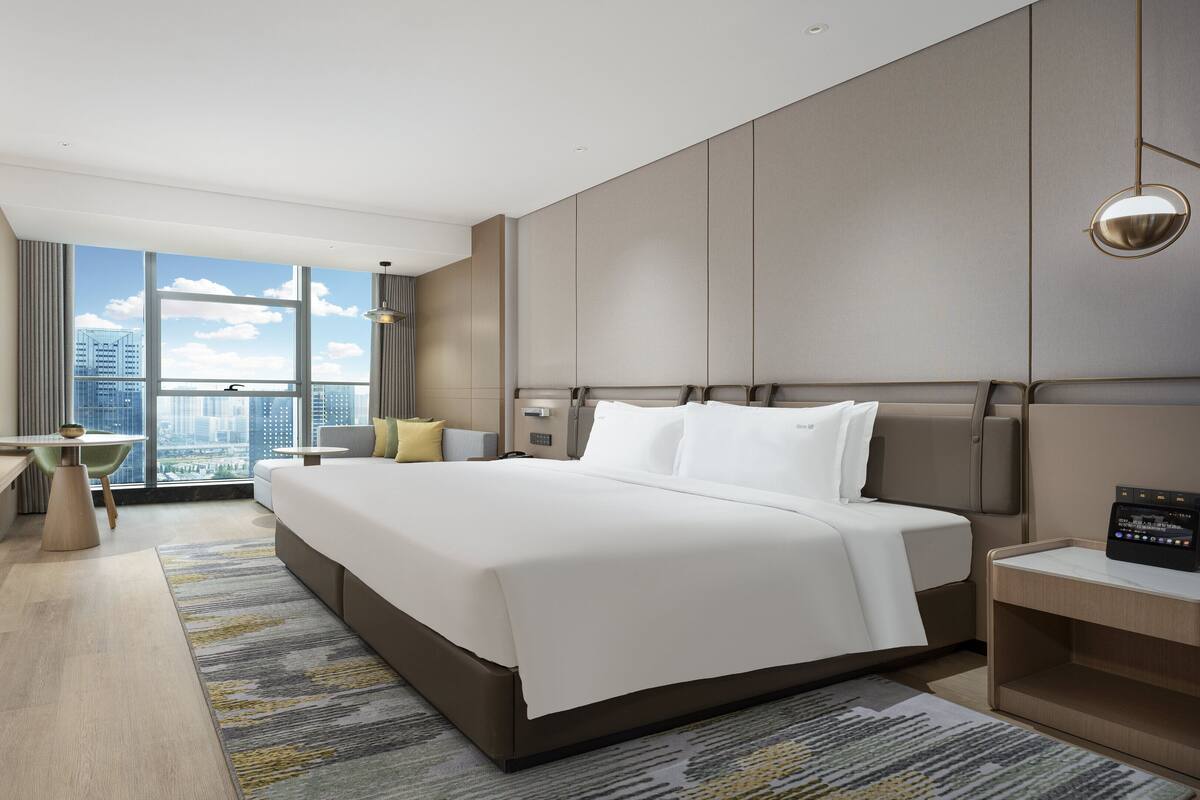 A modern hotel room with a large bed, a desk, and a view of the city.