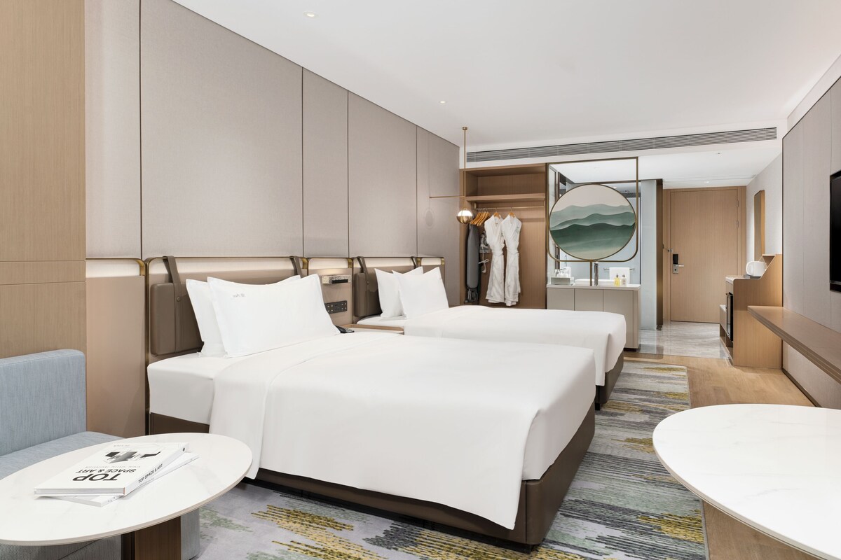 A hotel room with two beds, a sitting area with a table, a TV, and a bathroom visible through an open door.