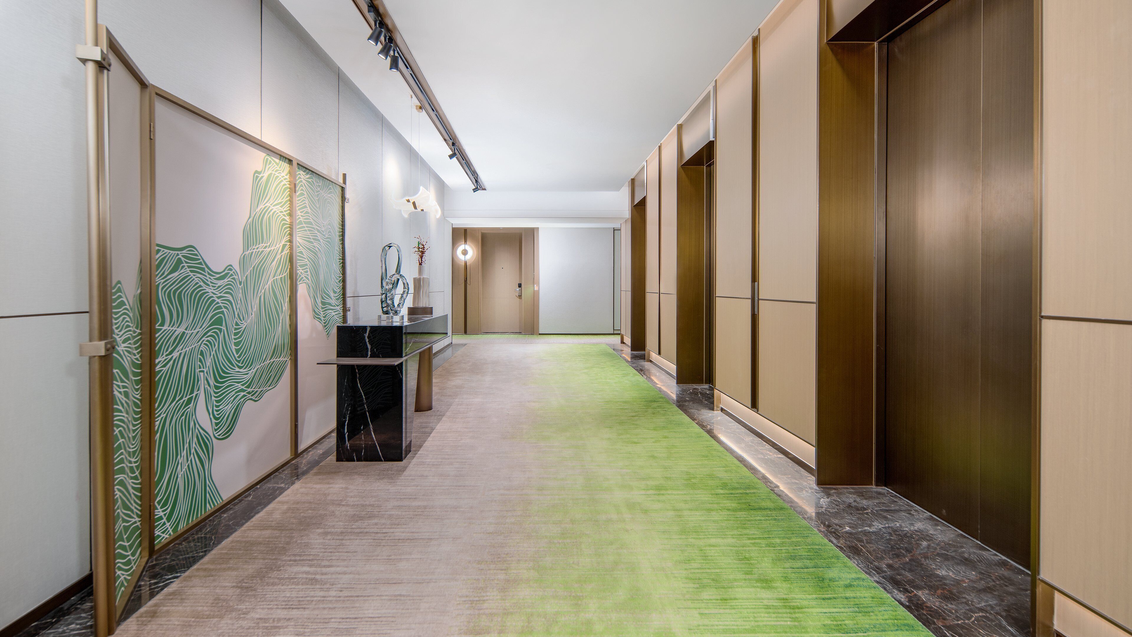 Un pasillo con alfombra verde, un mostrador de recepción y una pared con un diseño abstracto en tonos verdes.