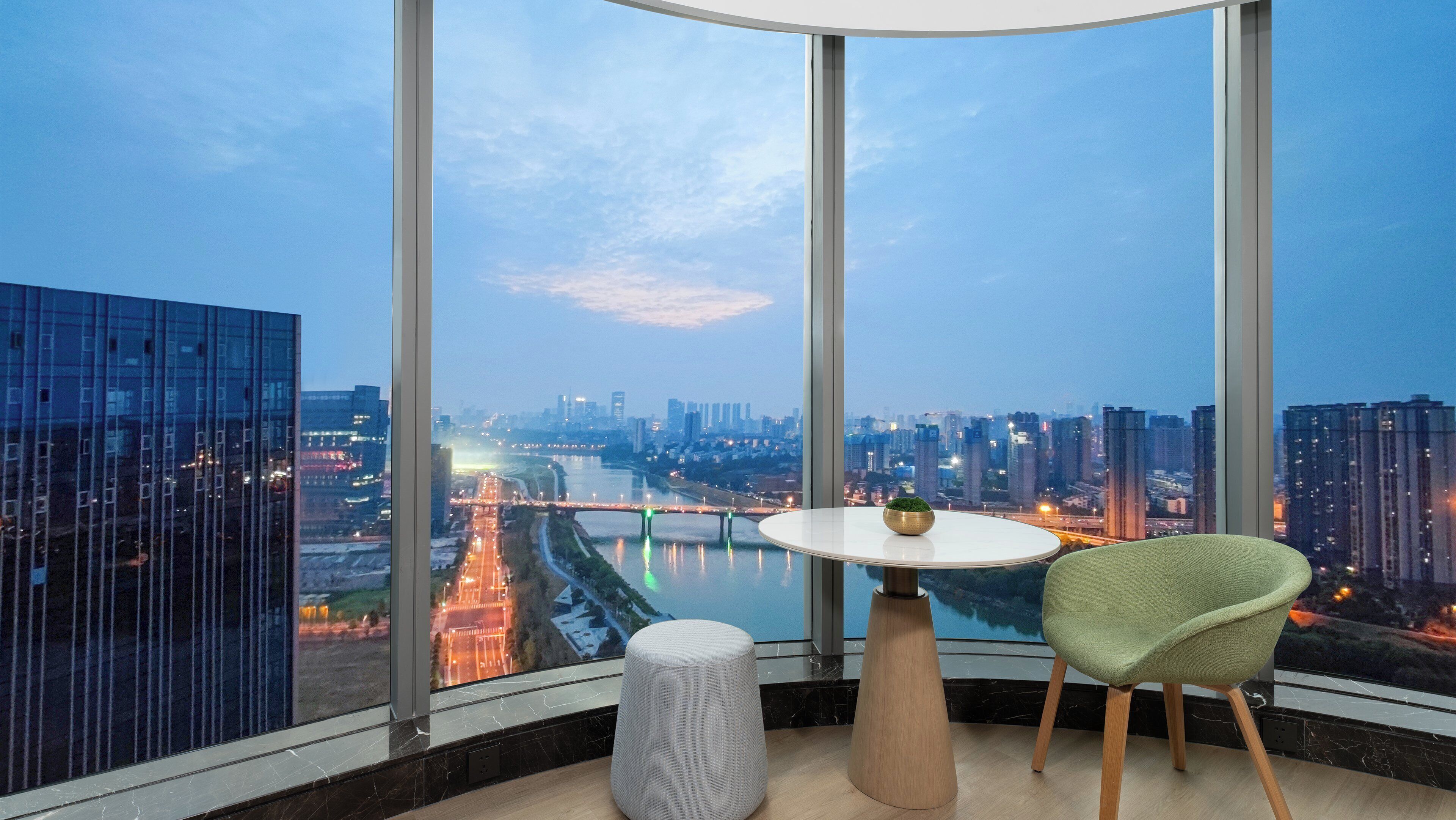 A modern room with a large window, a round table, a green chair, and a small stool.