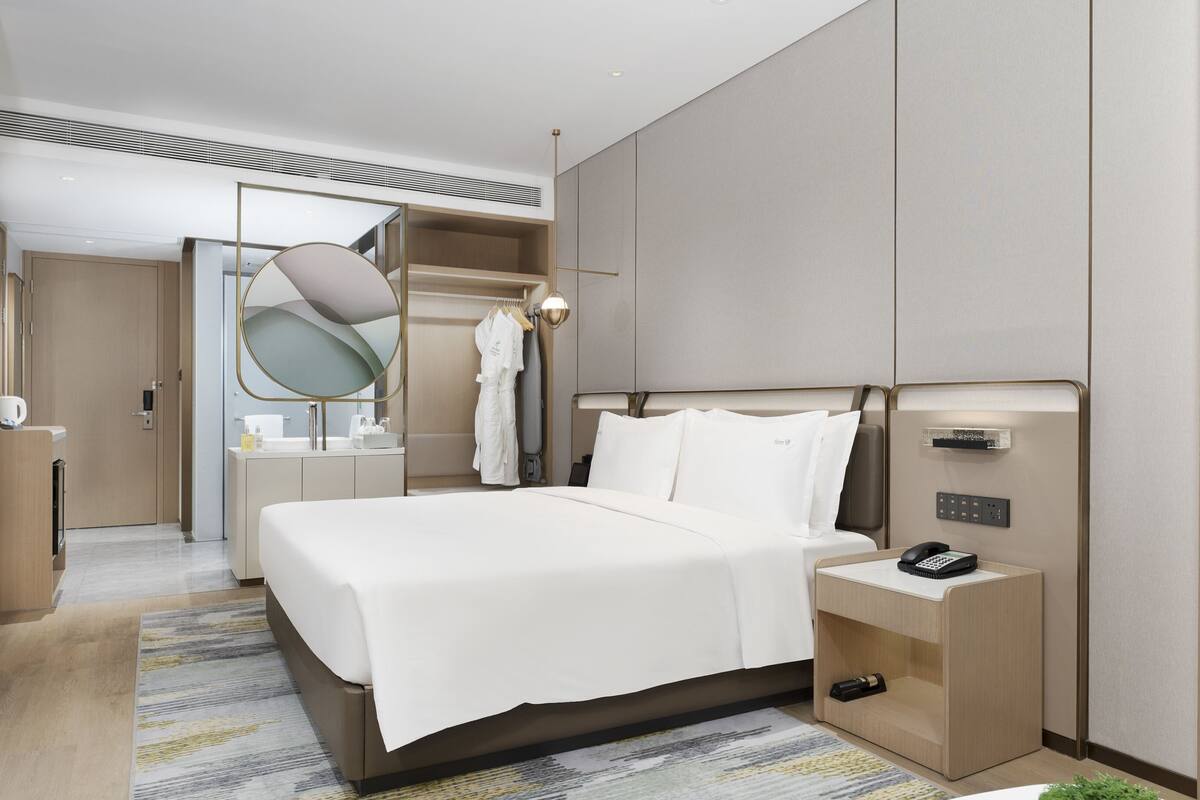 A modern hotel room with a large bed, bedside table, and a TV.