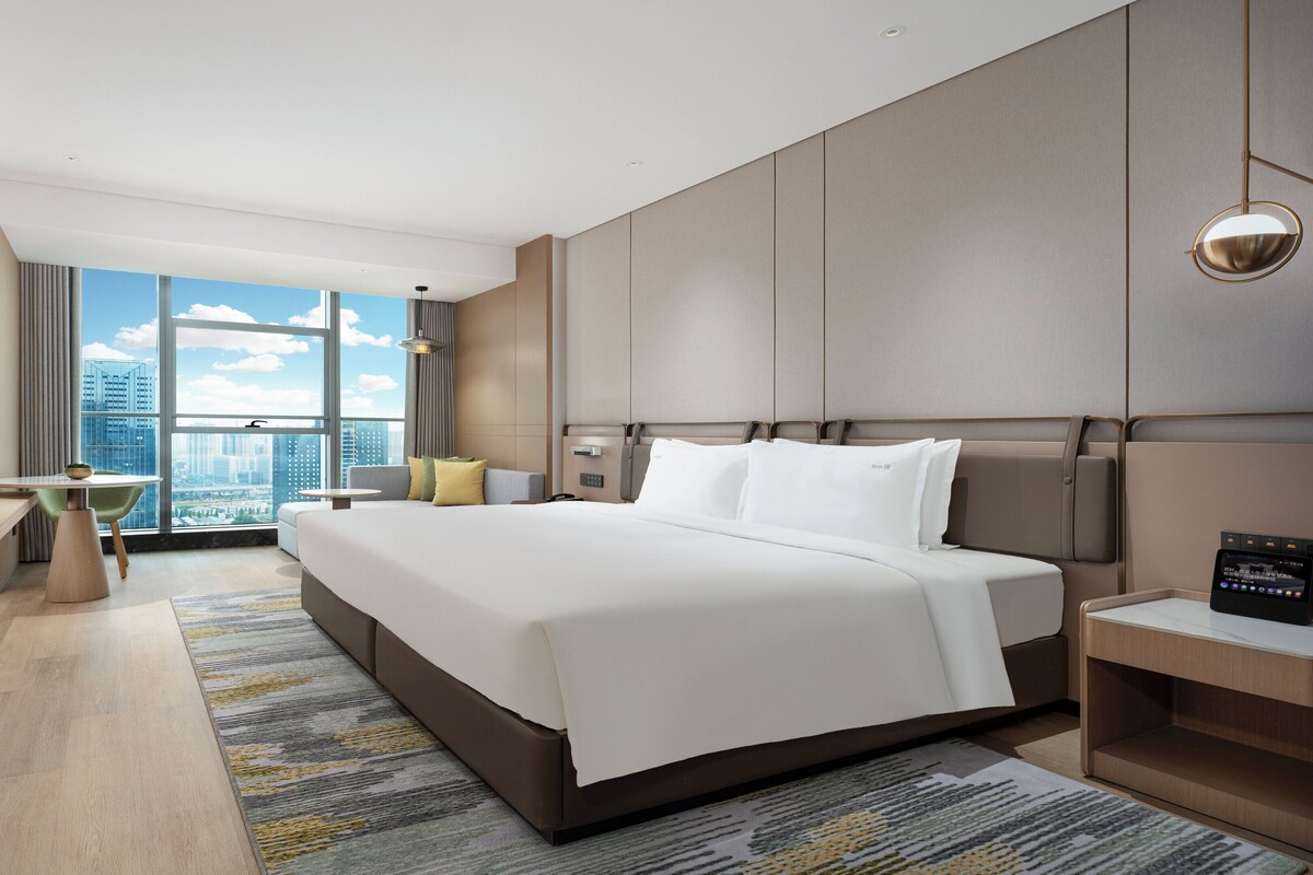 Een moderne hotelkamer met een groot bed, een bureau en uitzicht op de stad.