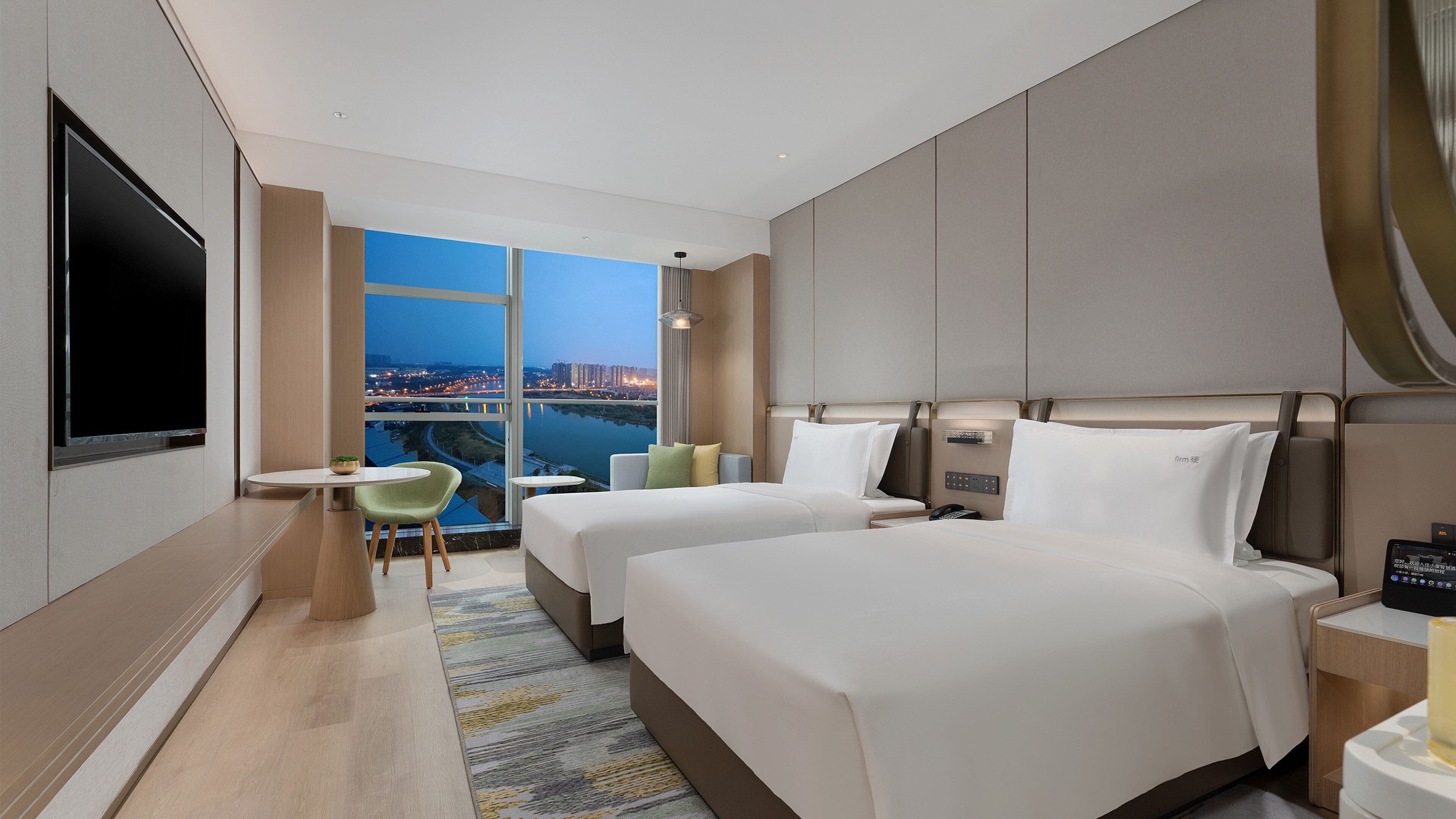 A hotel room with two beds, a TV, a desk, and a view of a cityscape.