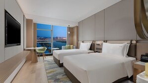 A hotel room with two beds, a TV, a desk, and a view of a cityscape.