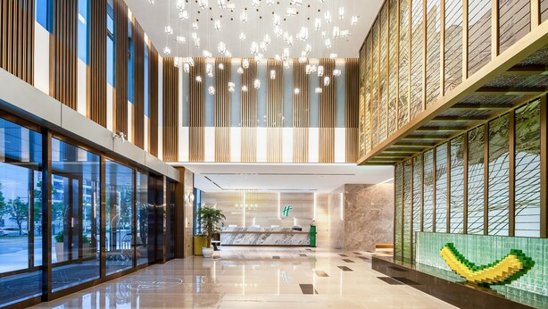 A modern hotel lobby with a reception desk, large windows, and a decorative wall with a pixelated design. - Holiday Inn Changsha Malanshan by IHG (Changsha)