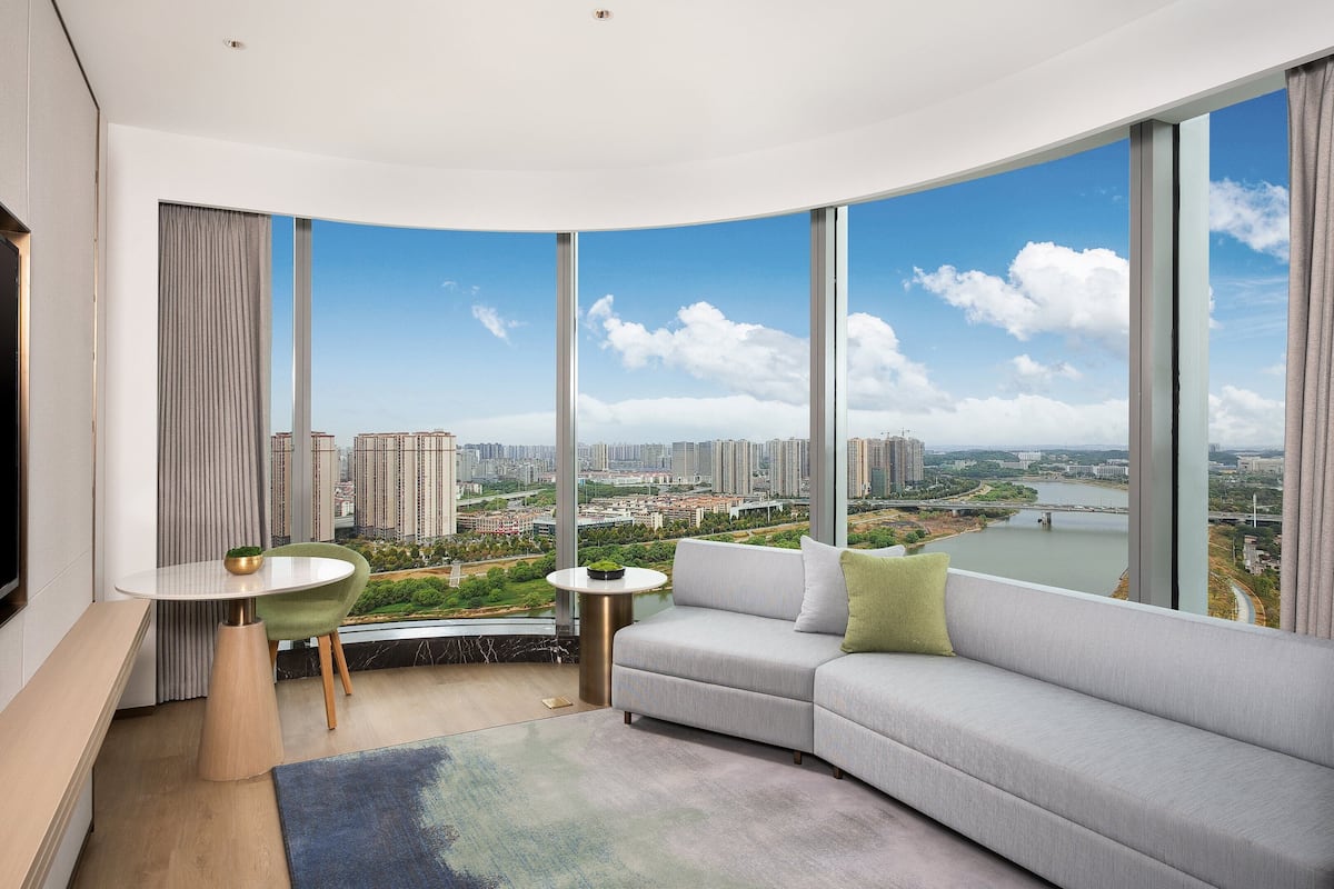 A modern living room with a curved view of a cityscape, a flat-screen TV, a round table, and a sofa.
