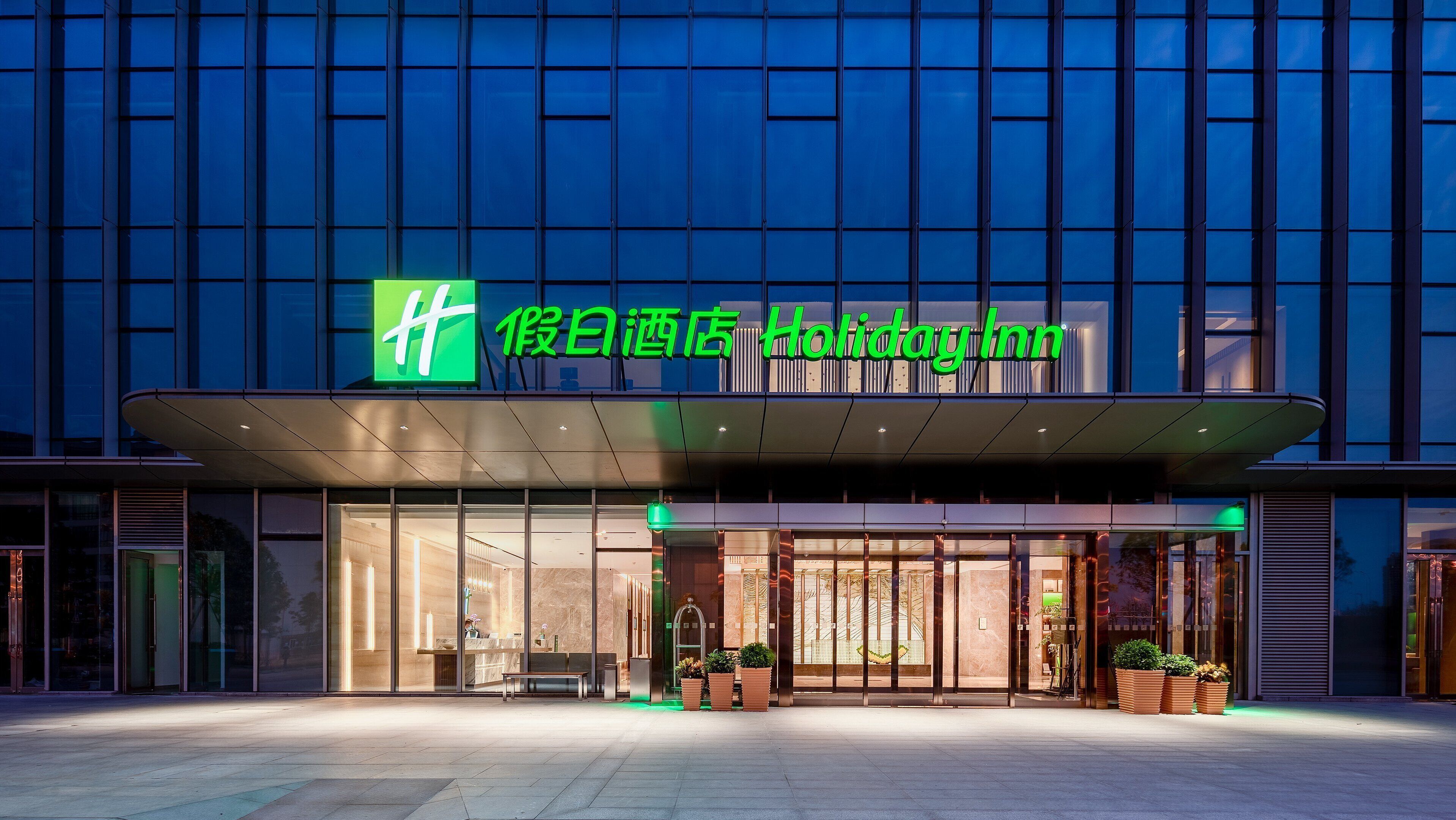 Ein Hotel mit modernem Glasfassadengrundriss, einem grün-weißen Logo und einem gut beleuchteten Empfangsbereich.