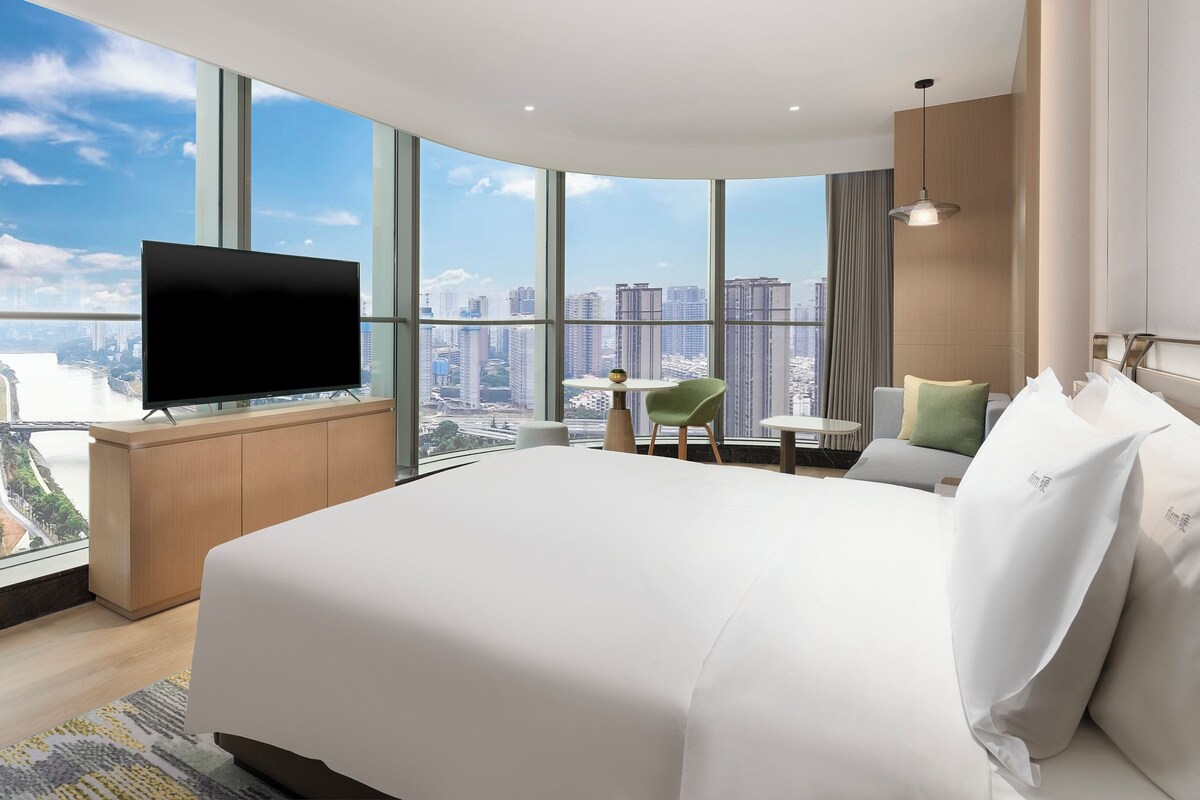 Een moderne hotelkamer met een groot bed, een flatscreen televisie, een klein tafeltje en een stoel.