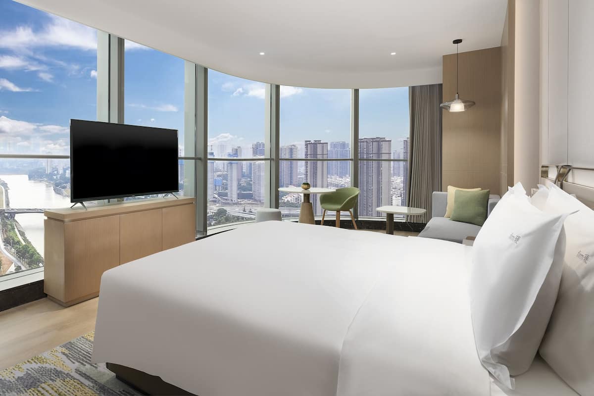 A modern hotel room with a large bed, a flat-screen TV, a small table, and a chair.