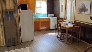 A compact kitchen with wooden cabinets, a refrigerator, a stove, and a dining table with chairs.