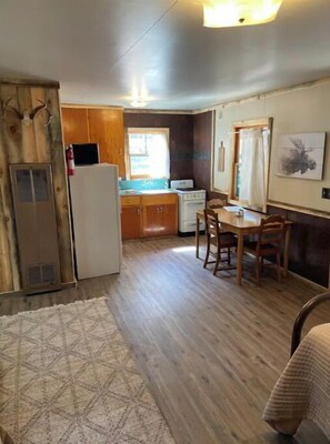 A compact kitchen with wooden cabinets, a refrigerator, a stove, and a dining table with chairs.