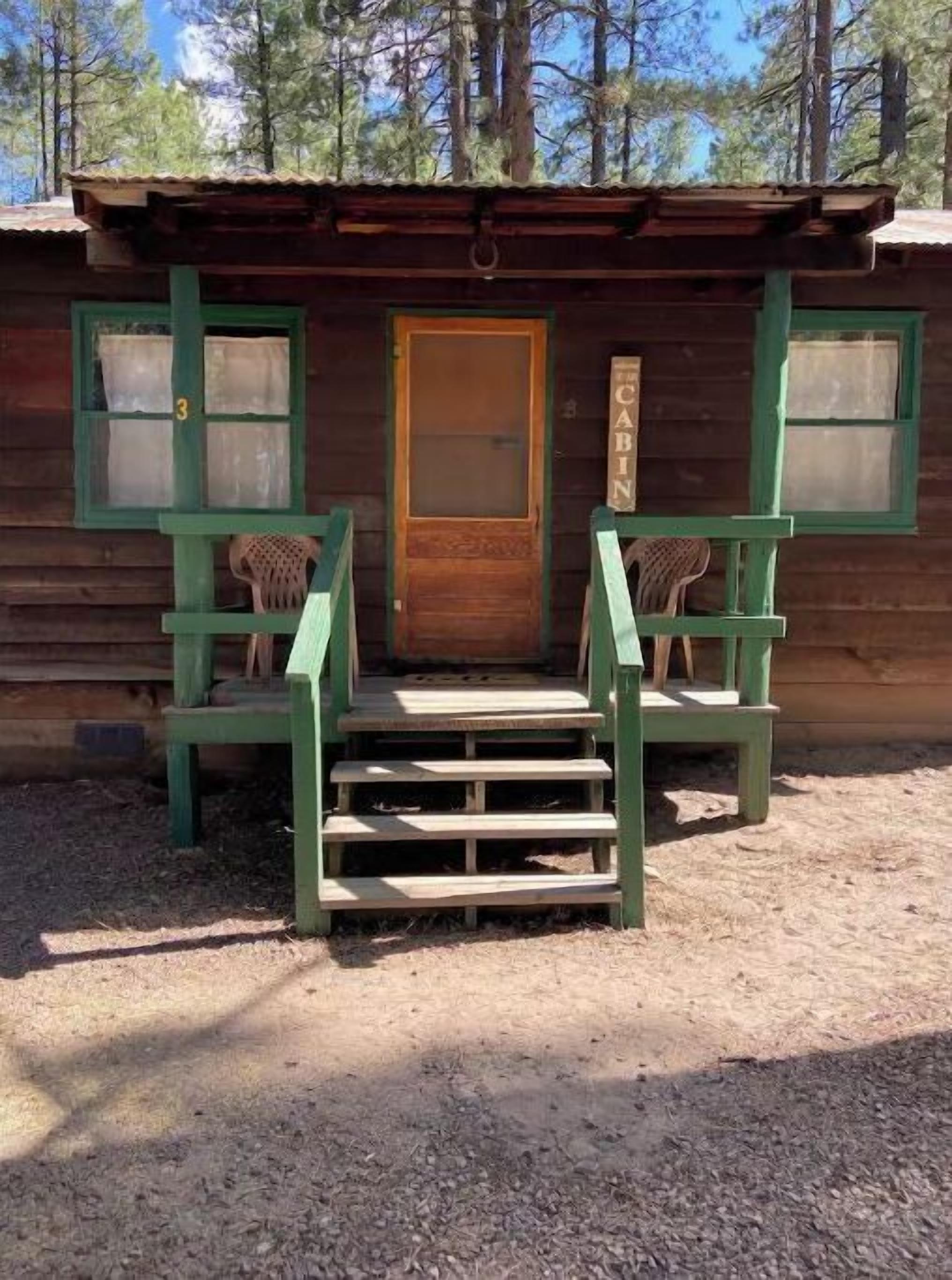 Une cabane avec une porte en bois, deux fenêtres et un escalier menant à une véranda équipée de deux chaises.