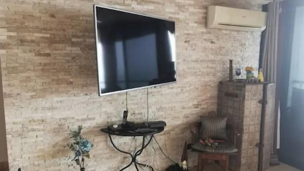 A living room with a flat-screen TV mounted on a brick wall, a small round table with a vase of flowers, a chair, and an air conditioning unit. - SPECTACULAR SEA VIEW WITH TERRACE ON BALBOA AV (Panama City)