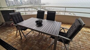 A balcony with a table and chairs, overlooking a cityscape and a body of water. - SPECTACULAR SEA VIEW WITH TERRACE ON BALBOA AV (Panama City)