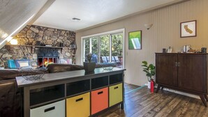 A cozy living room with a stone fireplace, a black leather sofa, and a colorful storage unit. - Hot Tub Hideaway  (Idyllwild-Pine Cove)