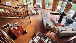 A spacious wooden interior with a high ceiling, large windows, a dining area with a table set for four, and a cozy seating area with a sofa and chairs. - Vista Greystone Lodge-Incredible view!! Streaming tvs! Wifi! Private! Sleeps 10! (Talking Rock)