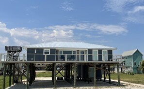 Ein Strandhaus mit überdachter Terrasse und einem separaten Obergeschoss.