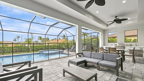 A spacious outdoor area with a pool, seating, and a kitchen area. - Brand NEW Construction, Beautiful Home, HEATED Pool in Highly Desirable SW Cape! (Cape Coral)