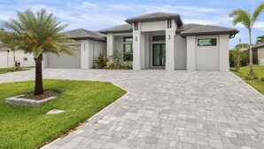A modern two-story house with a paved driveway, a palm tree, and a well-maintained lawn. - Brand NEW Construction, Beautiful Home, HEATED Pool in Highly Desirable SW Cape! (Cape Coral)