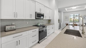 A modern kitchen with white cabinetry, stainless steel appliances, and a breakfast bar. - Brand NEW Construction, Beautiful Home, HEATED Pool in Highly Desirable SW Cape! (Cape Coral)