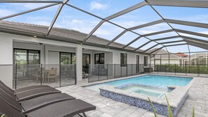 An outdoor swimming pool area with a glass enclosure, lounge chairs, and a patio with a tiled floor. - Brand NEW Construction, Beautiful Home, HEATED Pool in Highly Desirable SW Cape! (Cape Coral)