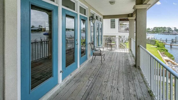 A covered wooden deck with a railing, overlooking a body of water and a dock. - Gated Community. Walking distance to the beach! Great Location! (Orange Beach)
