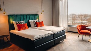A modern hotel room with a large bed, a view of the city, and a small table and chair. - Van der Valk Hotel Schiedam (Schiedam)