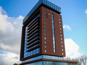 Un hôtel moderne, reconnaissable à son grand panneau « HÔTEL », à ses nombreux étages et à sa façade en verre.
