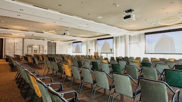 A conference room with rows of chairs, a projector screen, and a large window with a view of a building.