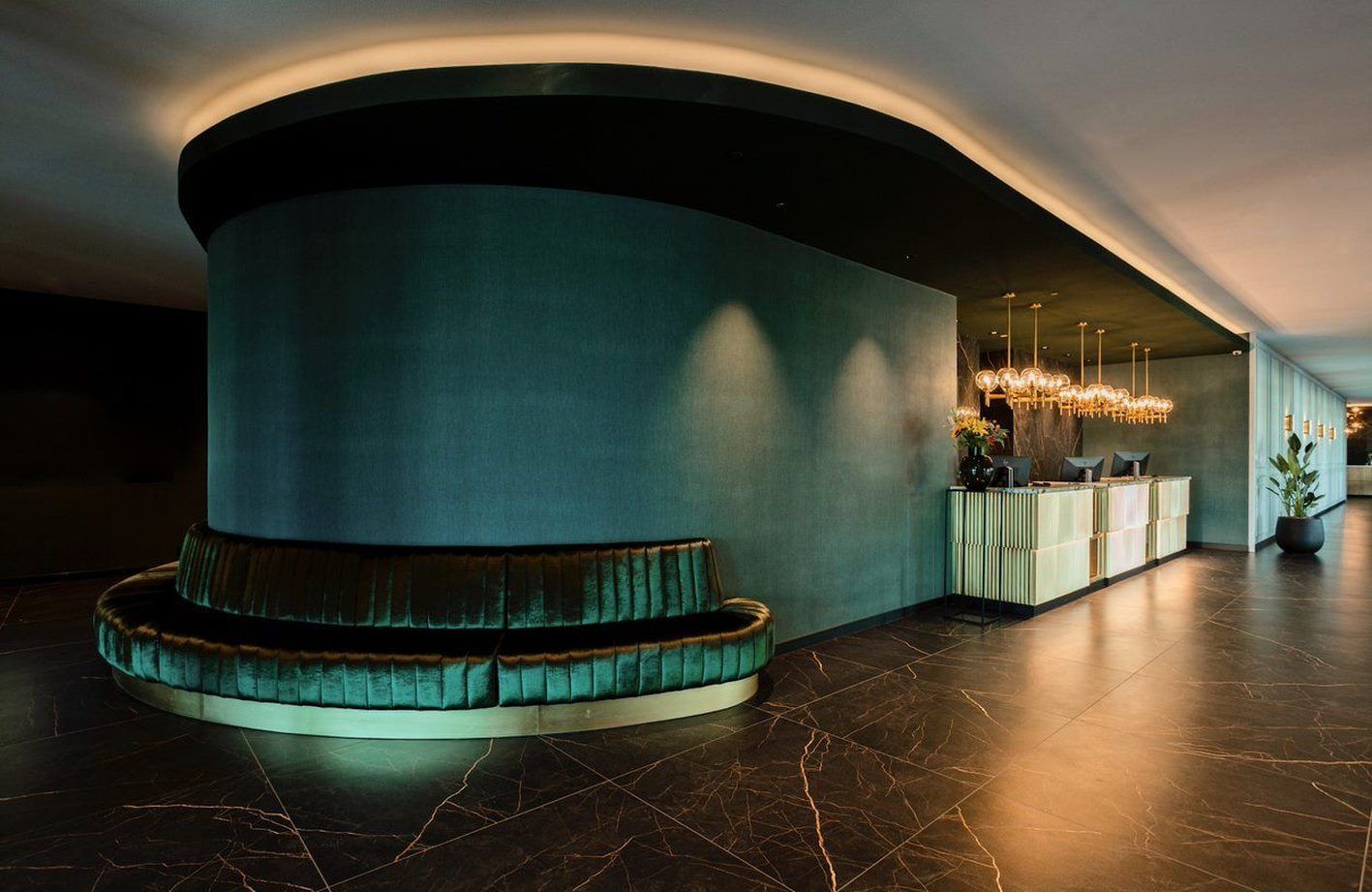 A lobby with a curved reception desk, a seating area with a plush chair, and a modern chandelier.