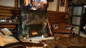 Un salón acogedor con chimenea de piedra, muebles de cuero y un trofeo de venado.